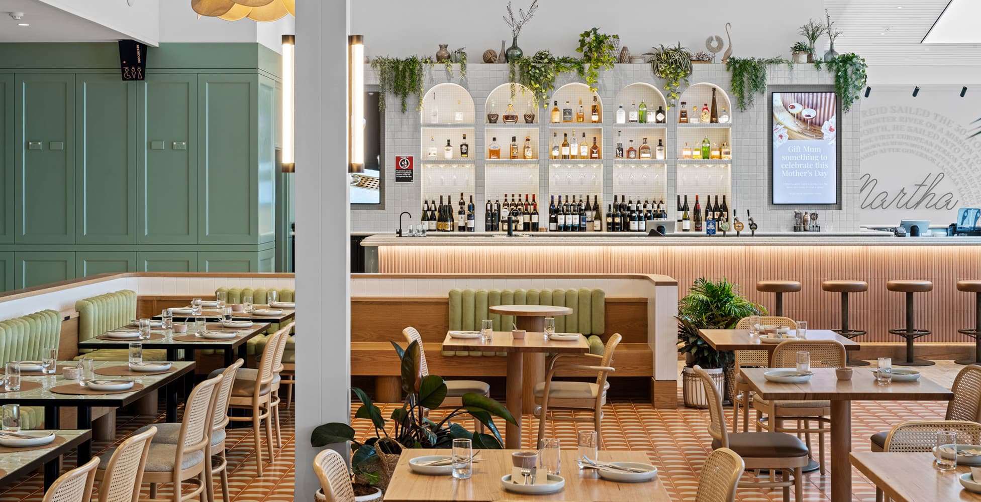 The Martha Drink and Dine restaurant interior featuring sage green banquettes, arched bottle display shelving, cane dining chairs, and a fluted timber bar with the Martha branding on the back wall.