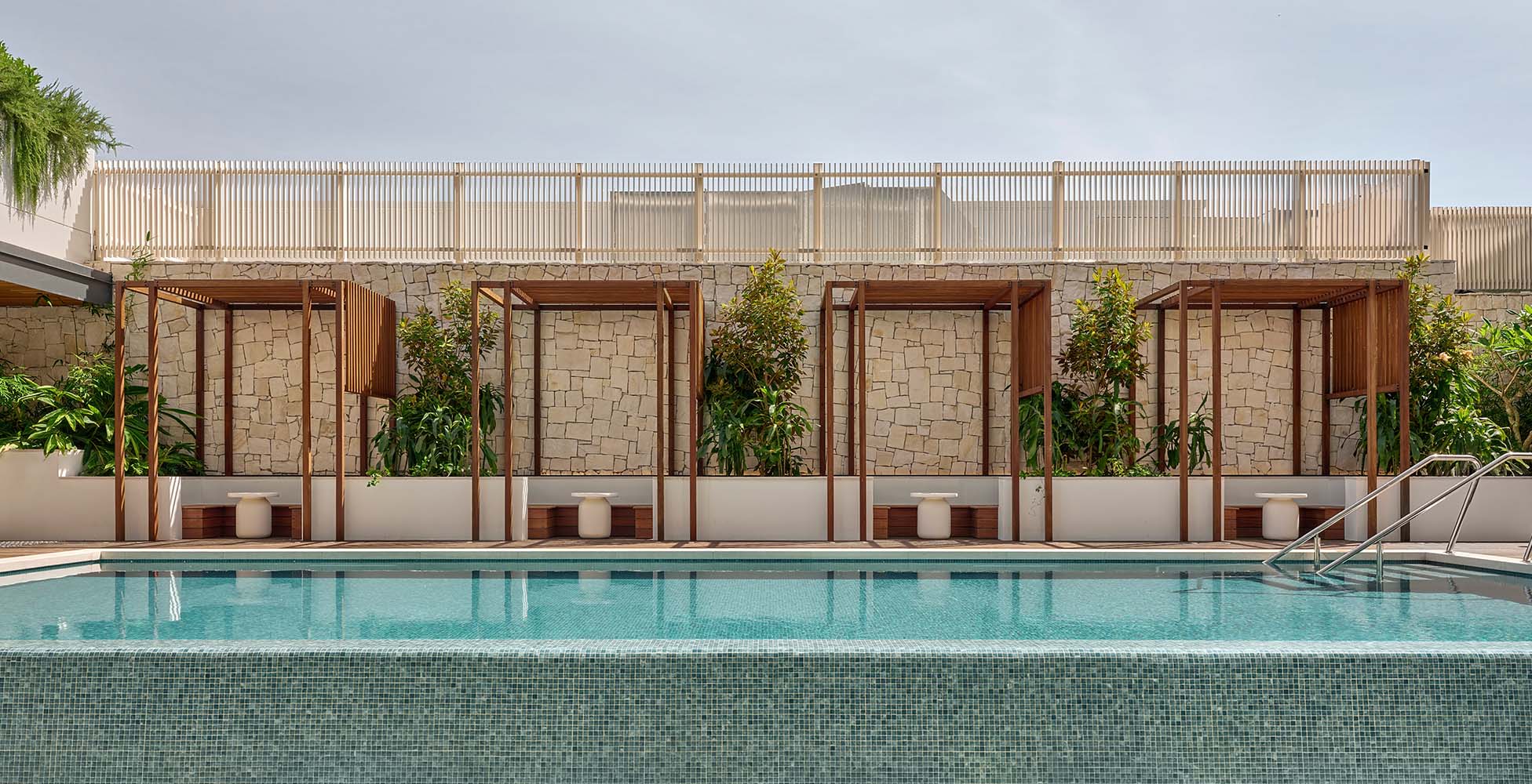 The hotel pool deck with timber cabanas, sandstone walls, and lush tropical planting — a resort amenity in the heart of Western Sydney.