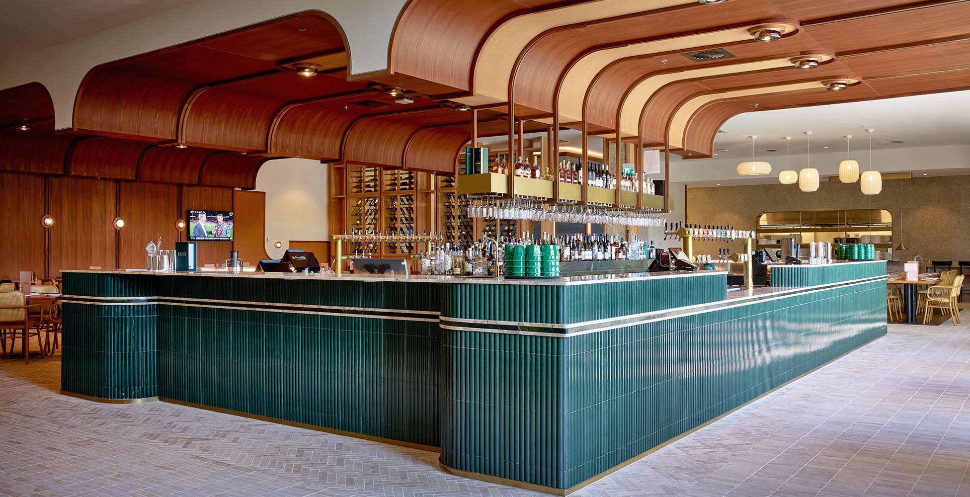 The new bar featuring deep green fluted tiles, timber batten ceiling, beer taps, and dining seating with natural light streaming through the arched windows.