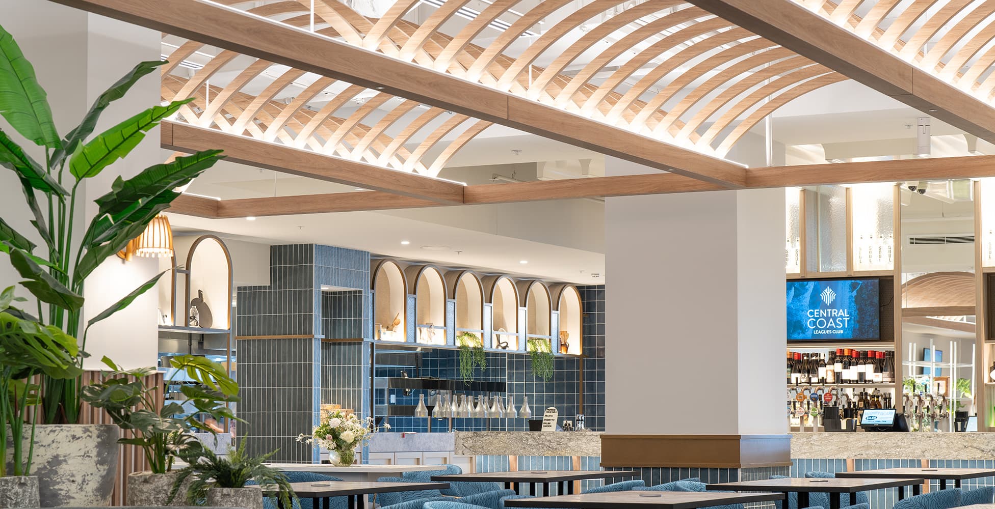 The main dining and bar area showing coastal-inspired arched features, timber ceiling lattice, and blue tile detailing throughout the space.