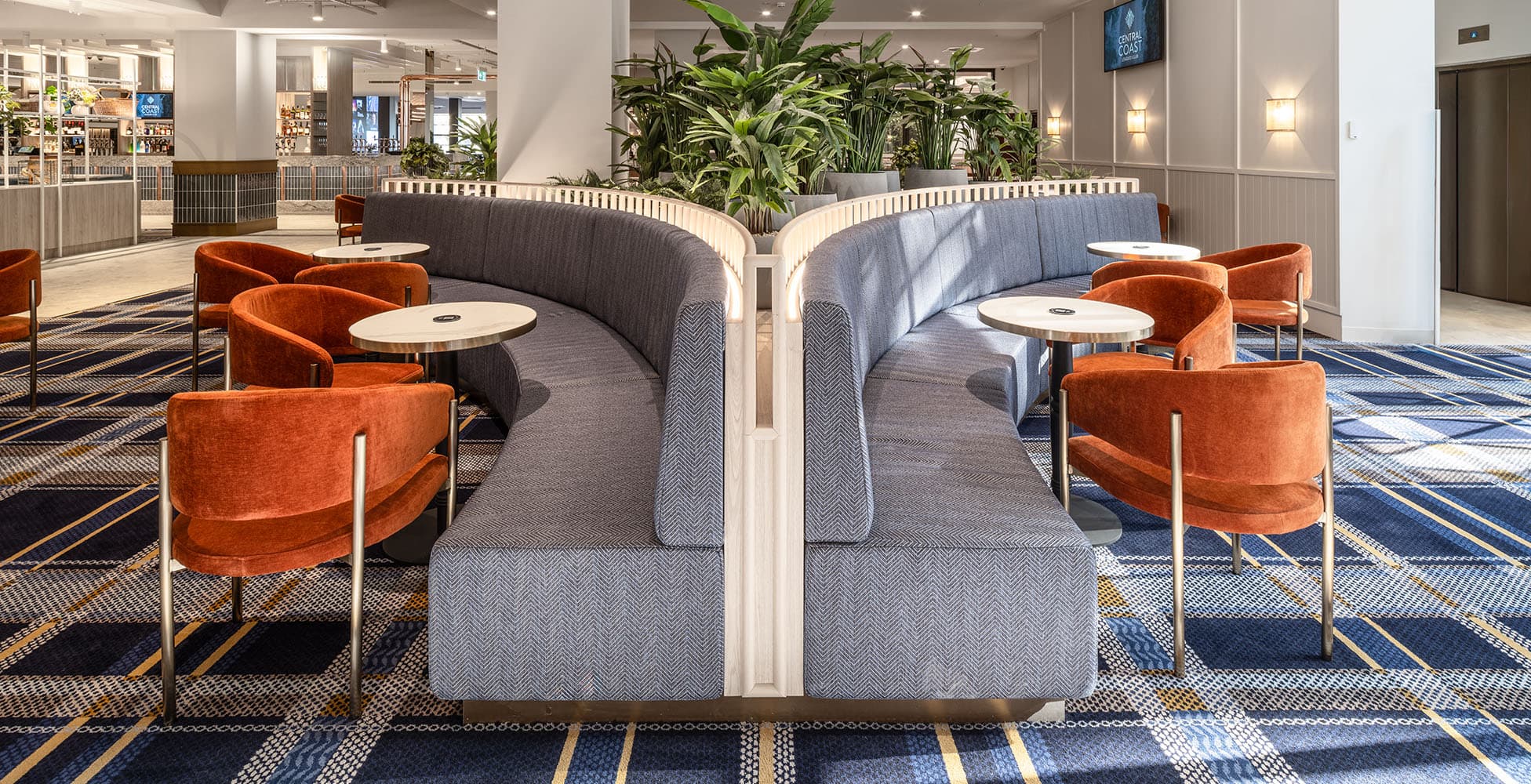 Lounge seating area with curved grey banquette, rust-coloured armchairs, and geometric carpet pattern showing the quality of interior finishes.