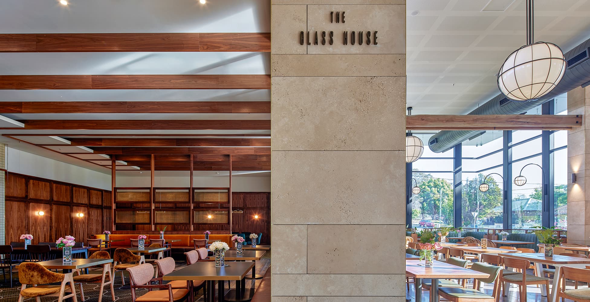 The Glass House dining area at Seven Hills RSL, where warm timber beams and stone columns frame a light-filled space with floor-to-ceiling windows overlooking landscaped gardens.