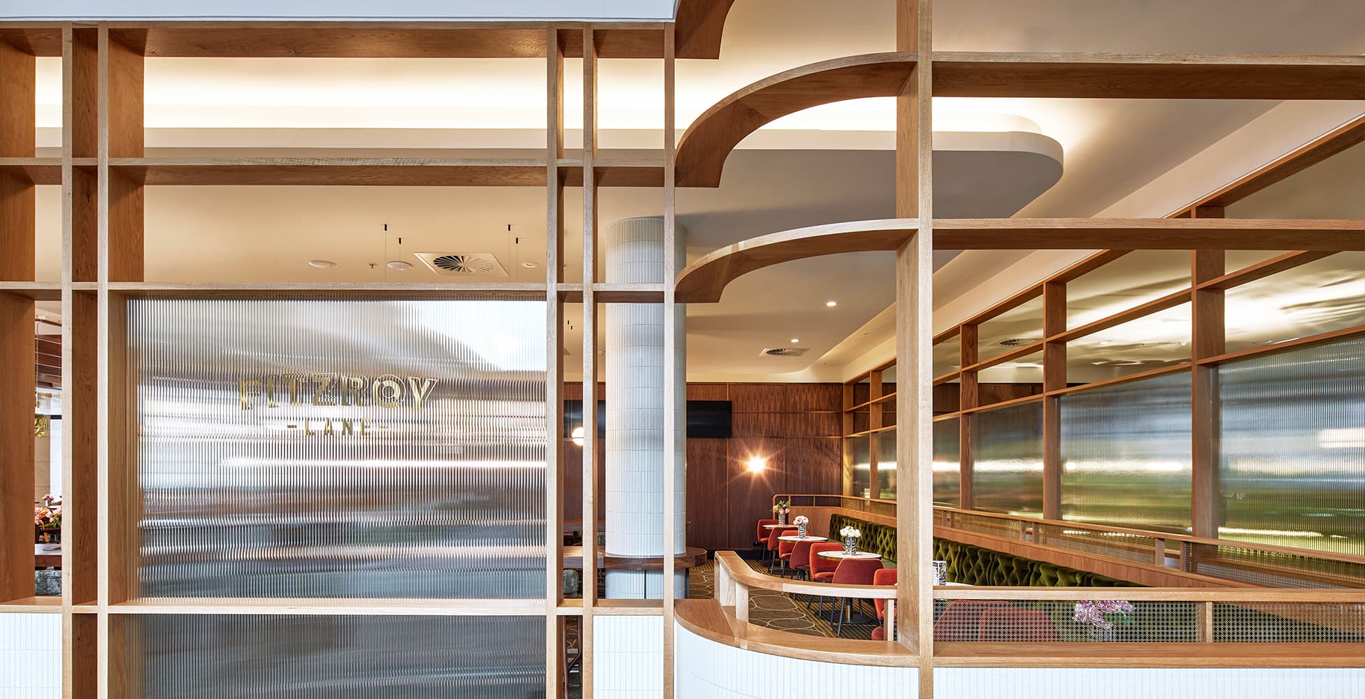 The Fitzroy Lane precinct at Seven Hills RSL, showcasing the elegant curved timber joinery, fluted glass partition, and warm material palette that define the dining experience.