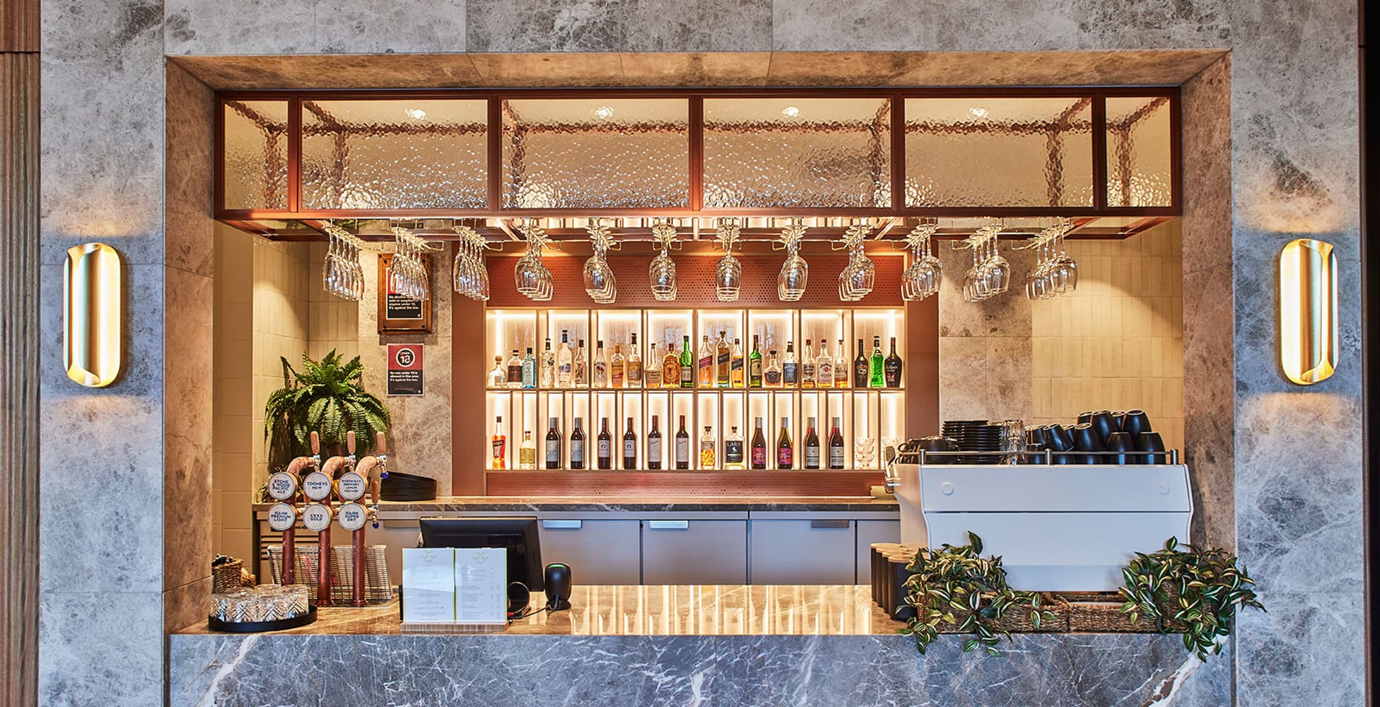 The redesigned bar at The Shellharbour Club featuring marble-effect stone, patterned glass overhead, copper and brass tones, and a warm material palette.